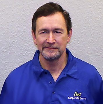 A man in a blue shirt is standing in front of a wall.