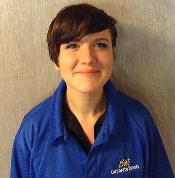 A woman in a blue shirt is standing in front of a wall.