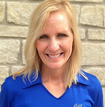 A woman in a blue shirt smiling in front of a stone wall.