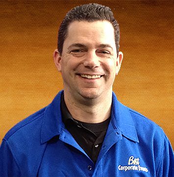 A man in a blue shirt smiling in front of a wooden background.