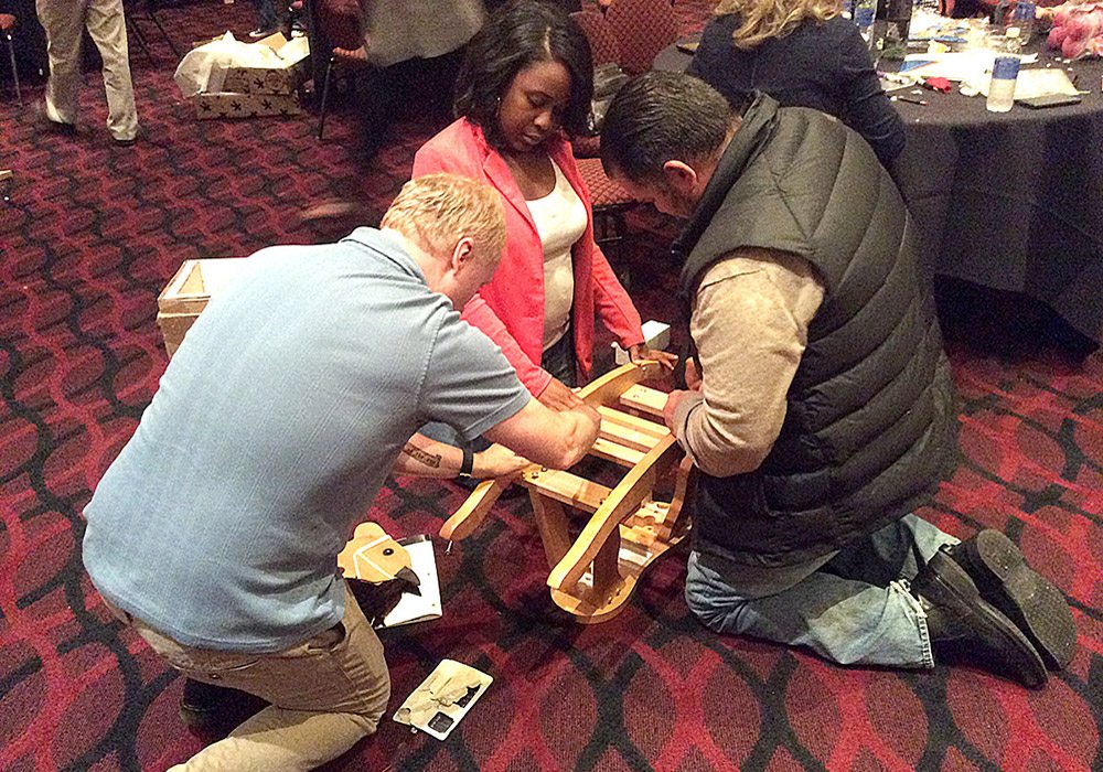 A group of people working on a wooden chair.