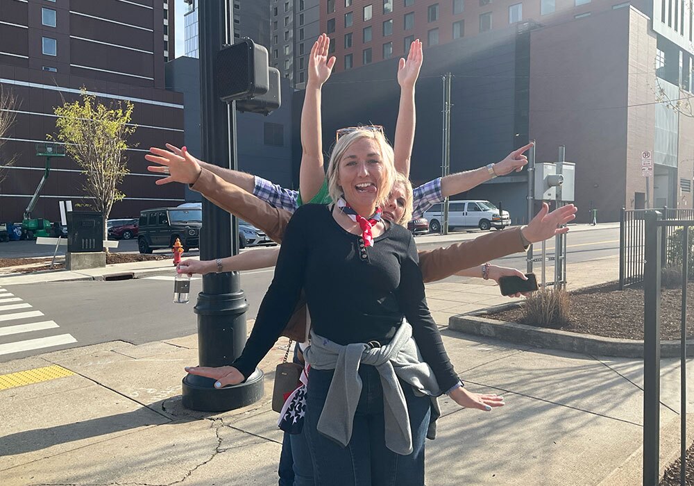 A person smiling with arms outstretched on a city street.