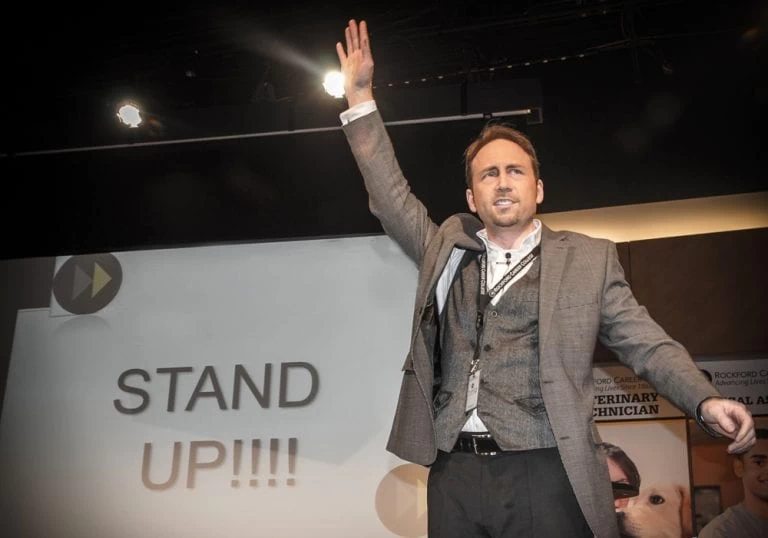 A man in a suit standing up in front of a screen.