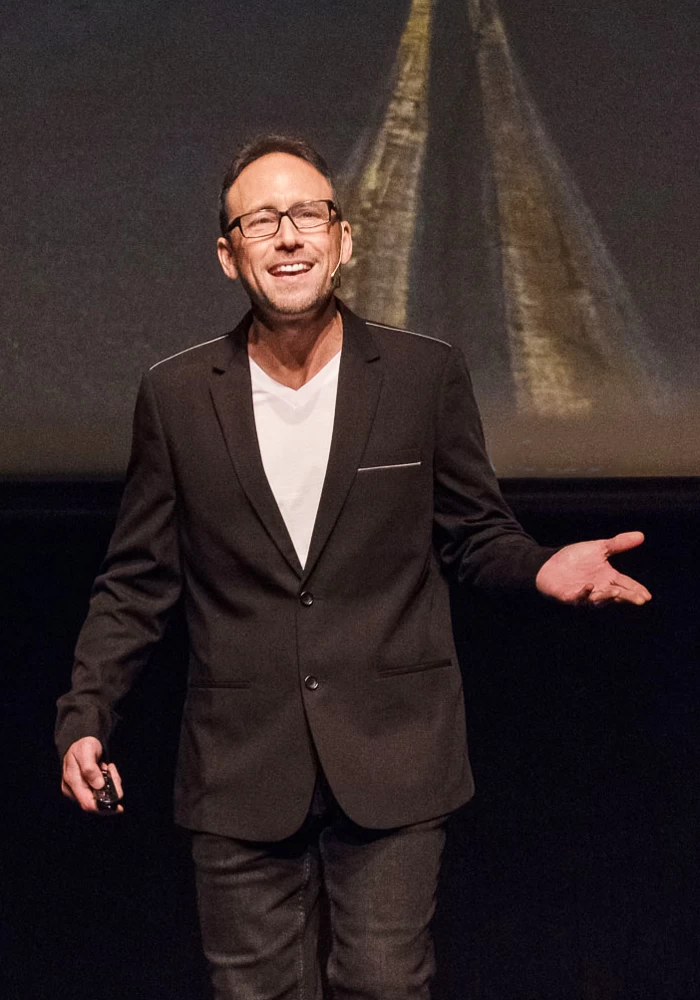 A man in a suit standing on a stage with a projection of a road.