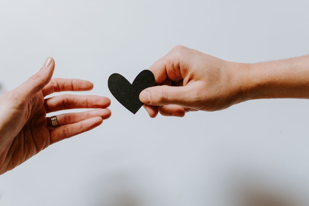 Two hands holding a black heart in each other's hands.