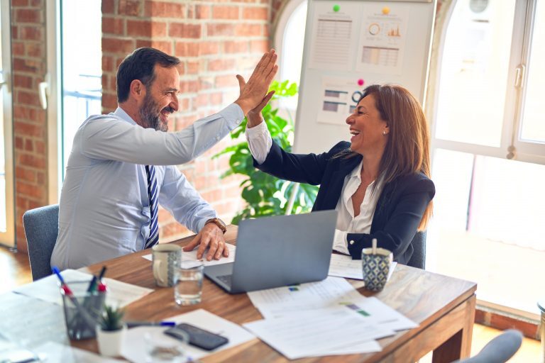 Two business people giving each other high fives in an office.